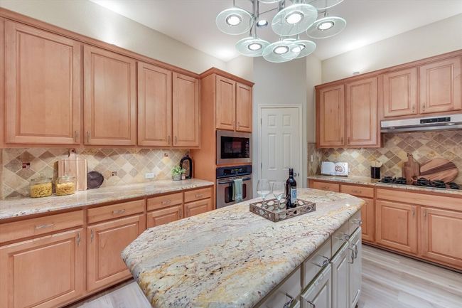 Kitchen with stainless steel oven, black gas stovetop, under cabinet range hood, built in microwave, and light stone countertops | Image 19