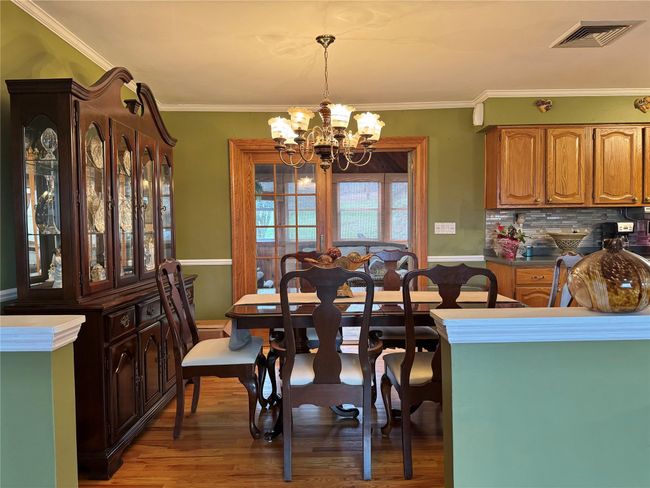 Dining area featuring light wood-type flooring, crown molding, a notable chandelier, and visible vents | Image 11