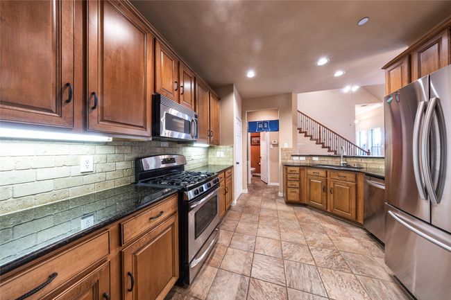 Kitchen with appliances with stainless steel finishes, decorative backsplash, recessed lighting, dark stone countertops, and brown cabinetry | Image 15