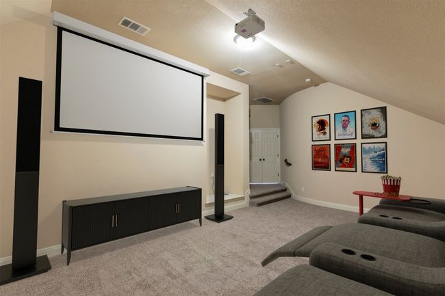 Carpeted home theater featuring vaulted ceiling, visible vents, and a textured ceiling | Image 23