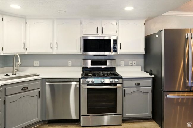 Kitchen featuring stainless steel appliances, a sink, gray cabinetry, light wood finished floors, and crown molding | Image 11