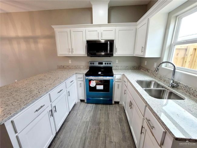 Kitchen with white cabinets, a sink, wood finished floors, light stone countertops, and range with electric stovetop | Image 5