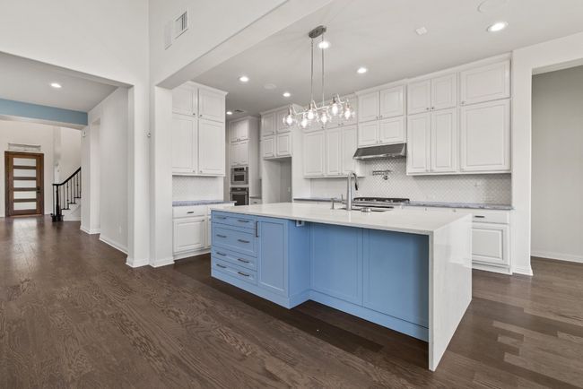 Kitchen featuring under cabinet range hood, white cabinets, tasteful backsplash, dark wood-style floors, and recessed lighting | Image 4