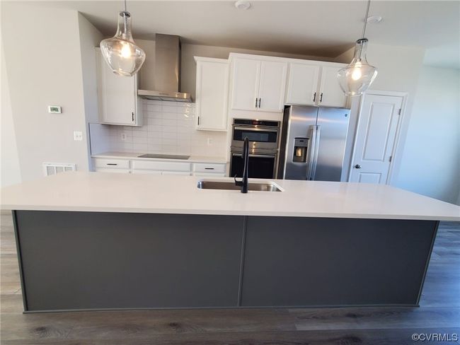 Kitchen featuring wall chimney range hood, stainless steel appliances, white cabinets, hardwood flooring, light countertops, hanging light fixtures, and backsplash | Image 10