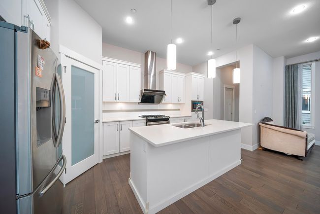 Kitchen featuring appliances with stainless steel finishes, a sink, wall chimney exhaust hood, dark wood-style floors, and light countertops | Image 13