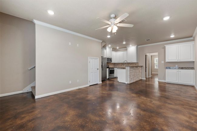 Unfurnished living room with concrete floors, a ceiling fan, ornamental molding, recessed lighting, and stairs | Image 7