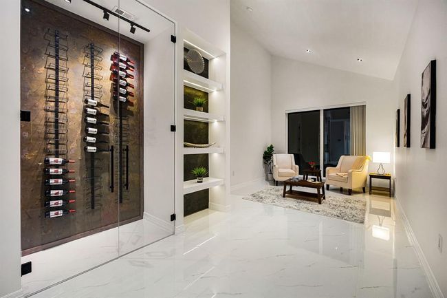 Step into this elegantly curated lounge featuring a stunning glass-enclosed wine display, custom lit shelving, and glossy marble-look tile floors. Perfect for entertaining or relaxing in style, this sophisticated space combines luxury with comfort, creating the ultimate setting for elevated living. | Image 20