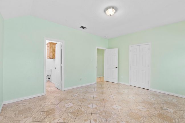 Unfurnished bedroom featuring baseboards, a closet, connected bathroom, vaulted ceiling, and light tile patterned floors | Image 13