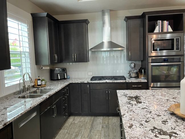 Kitchen with wall chimney range hood, stainless steel appliances, quartz countertops, and a wealth of natural light | Image 13