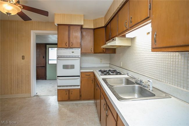 Kitchen featuring white appliances, a warming drawer, under cabinet range hood, brown cabinetry, and light countertops | Image 18