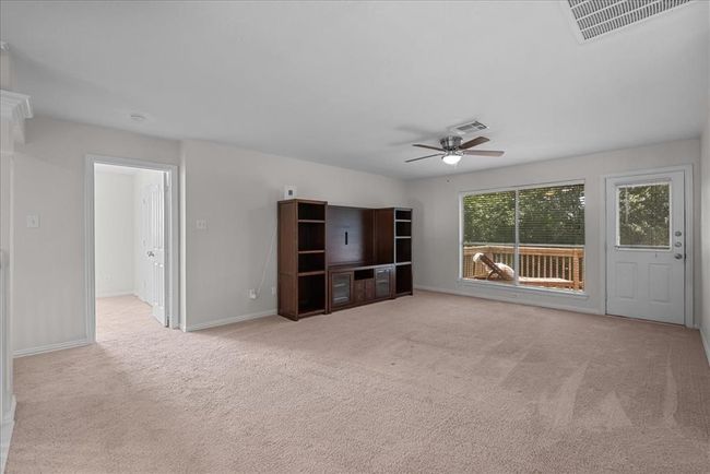 This spacious game room features neutral carpeting, a ceiling fan, and a large window with a view of the deck and lake. | Image 22