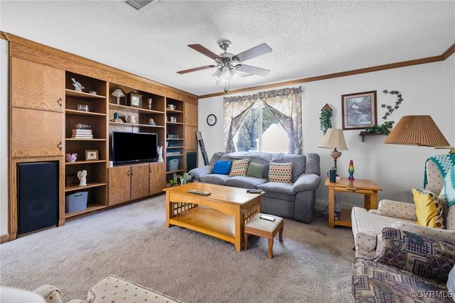 Living room featuring light carpet, a ceiling fan, a textured ceiling, and ornamental molding | Image 8