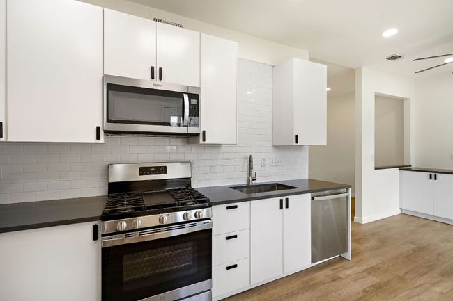 Kitchen featuring appliances with stainless steel finishes, dark countertops, light wood finished floors, tasteful backsplash, and recessed lighting | Image 10