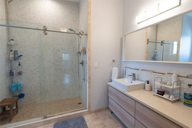 Bathroom with a stall shower, vanity, tile patterned floors, and decorative backsplash | Image 21