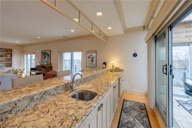 Bar in living room, adjacent to sun room featuring light wood finished floors, light stone countertops, a sink, ornamental molding, and white cabinets | Image 18