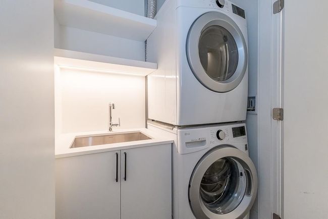 Laundry room featuring cabinet space, stacked washing maching and dryer, and a sink | Image 25