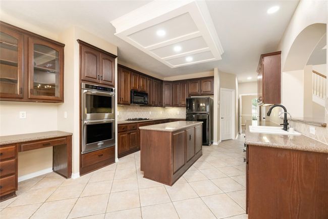The spacious kitchen has a functional layout, featuring a central island, ample counter space and a built-in desk offering a blend of functionality and sophistication. | Image 14