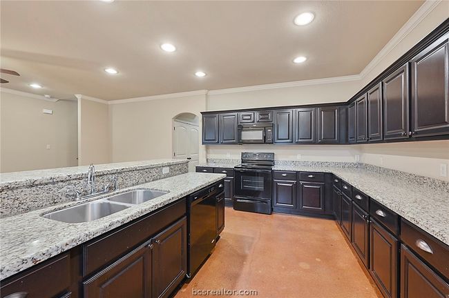 Kitchen with arched walkways, a sink, finished concrete flooring, crown molding, and black appliances | Image 4