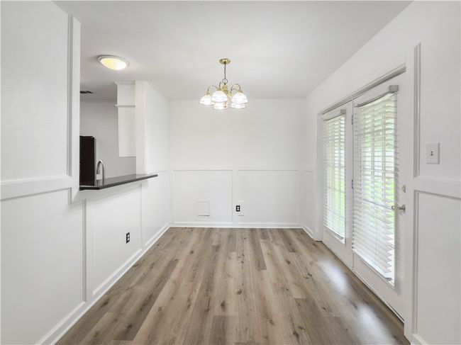 Unfurnished dining area featuring light wood-style flooring, wainscoting, a decorative wall, and a chandelier | Image 9