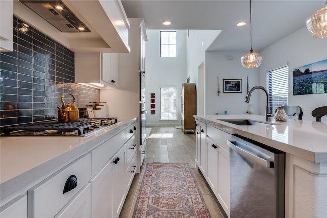 Kitchen with stainless steel appliances, light countertops, white cabinets, hanging light fixtures, and recessed lighting | Image 14