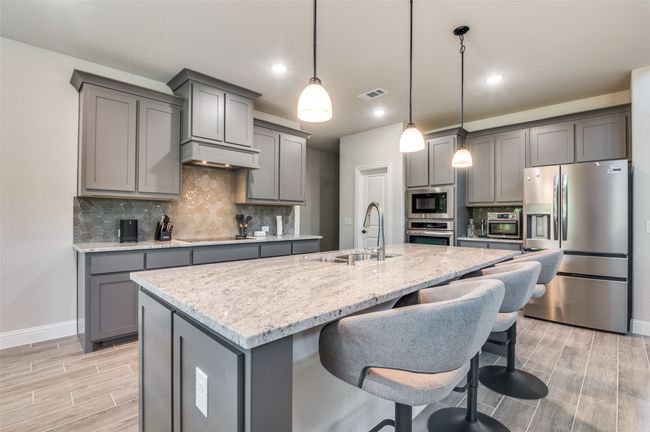 Kitchen featuring gray cabinetry, stainless steel appliances, an island with sink, tasteful backsplash, and wood finish floors | Image 12