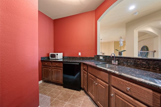 Kitchen featuring black dishwasher, light tile patterned flooring, a textured wall, dark stone countertops, and arched walkways | Image 31