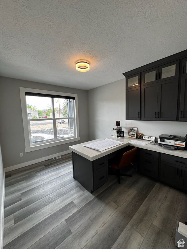 Office area with wood finished floors, built in desk, a textured ceiling, and baseboards | Image 9