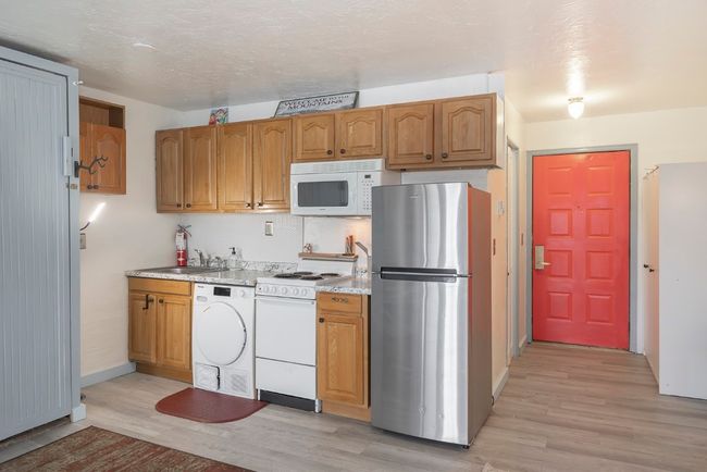 Kitchen featuring white appliances, washer / dryer, light wood-type flooring, and brown cabinets | Image 12