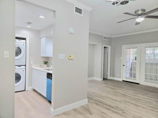 Laundry room featuring stacked washing machine and dryer, light wood-style floors, ornamental molding, ceiling fan, and baseboards | Image 4