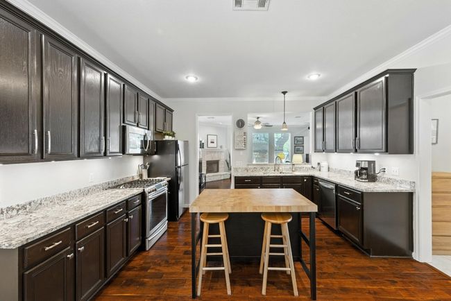 Kitchen with stainless steel appliances, a breakfast bar area, dark wood-style flooring, crown molding, and ceiling fan | Image 9
