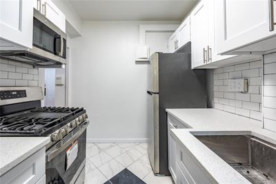 Kitchen with decorative backsplash, appliances with stainless steel finishes, light tile patterned flooring, and white cabinets | Image 2