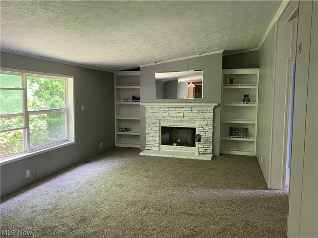 Unfurnished living room featuring a textured ceiling, ornamental molding, dark colored carpet, and a fireplace | Image 3