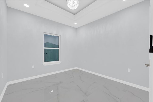 This photo showcases a bright, modern room with light gray walls and glossy tile flooring. It features a window providing natural light, recessed lighting, and a stylish ceiling fixture, creating a clean and contemporary space. | Image 24
