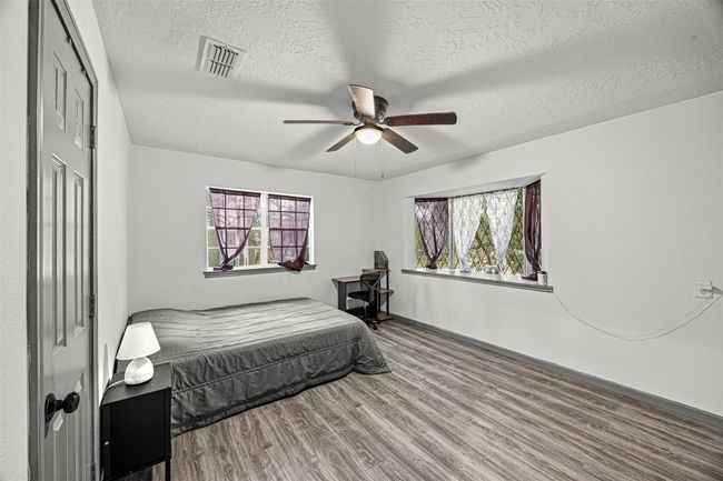 This room is bright and spacious with two windows allowing natural light. It features a ceiling fan, laminate flooring, and neutral walls. | Image 23