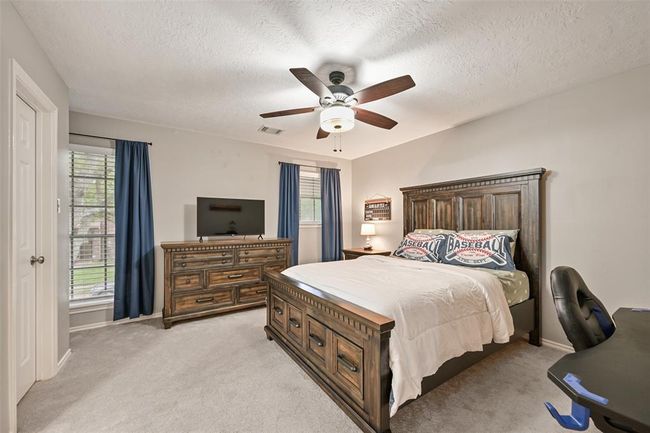 The first of two spacious secondary bedrooms on the second floor offers plush carpet, neutral tones, and great natural light from dual windows. A ceiling fan, walk-in closet, & en suite bath add comfort and convenience. | Image 18