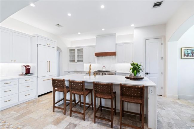 Kitchen with wall chimney range hood, arched walkways, stone tile floors, a breakfast bar area, and light countertops | Image 8