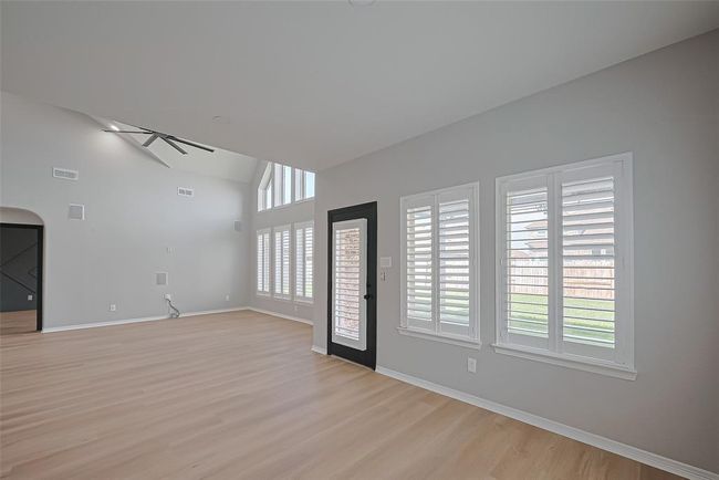 This spacious room features high ceilings, light wood flooring, and large windows with plantation shutters, providing abundant natural light. An elegant ceiling fan and a modern door complete the airy, open atmosphere. | Image 15