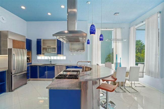The modern kitchen features a 4-burner gas range, stainless appliances, bar style dining, and upgrades including pendant lighting, wine refrigerator and convenient pot filler. | Image 8