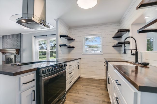 Kitchen featuring open shelves, stainless steel electric range oven, butcher block countertops, island range hood, and ornamental molding | Image 13