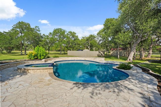 View of swimming pool featuring a pool with connected hot tub, a patio, and view of wooded area | Image 32