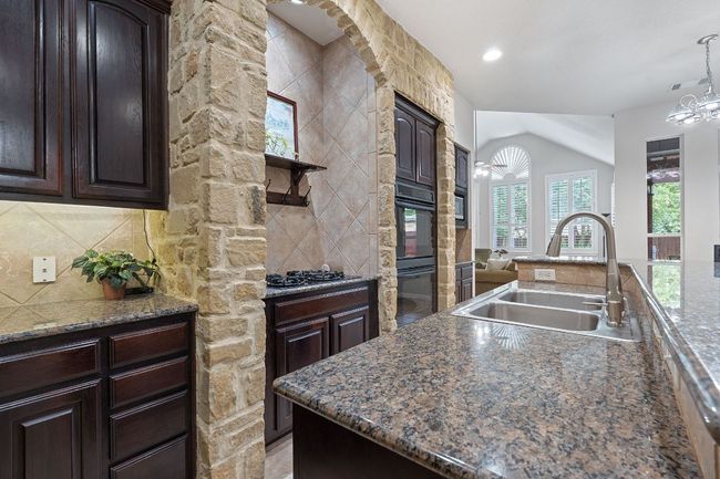 Kitchen featuring a sink, dark brown cabinetry, backsplash, decorative light fixtures, and black appliances | Image 7