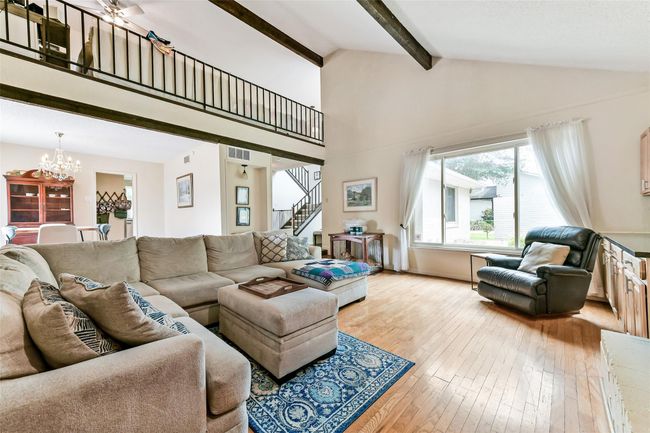 Spacious living room with high ceilings, exposed beams, and abundant natural light from a large window. | Image 11