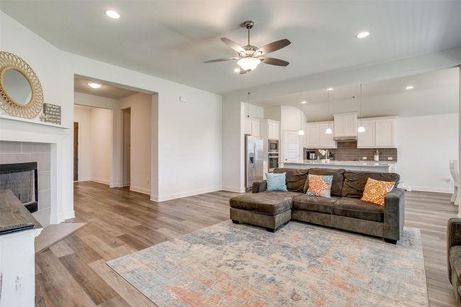 Living area with a ceiling fan, light wood finished floors, a tile fireplace, baseboards, and recessed lighting | Image 8