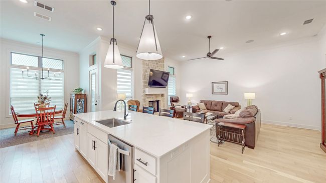 Kitchen with stainless steel dishwasher, light wood-type flooring, a stone fireplace, a chandelier, and crown molding | Image 8