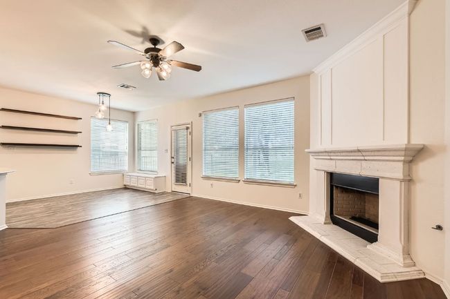 Unfurnished living room with a ceiling fan, a fireplace with raised hearth, and dark wood-style flooring | Image 10