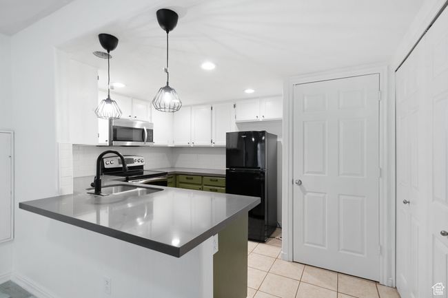 Kitchen featuring backsplash, white cabinetry, stainless steel appliances, a peninsula, and light tile patterned floors | Image 7