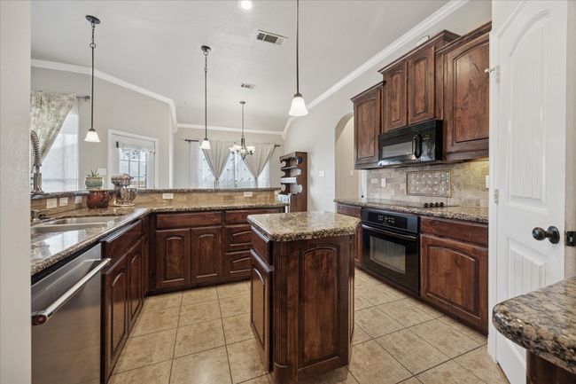 Kitchen featuring black appliances, crown molding, tasteful backsplash, a kitchen island, and stone counters | Image 8