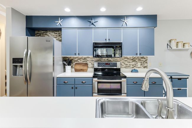 Kitchen with blue cabinets, light countertops, decorative backsplash, stainless steel appliances, and a sink | Image 5