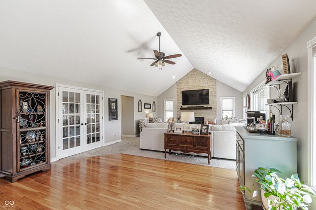 living room with a ceiling fan, a stone fireplace, french doors, light wood finished floors, and lofted ceiling | Image 6