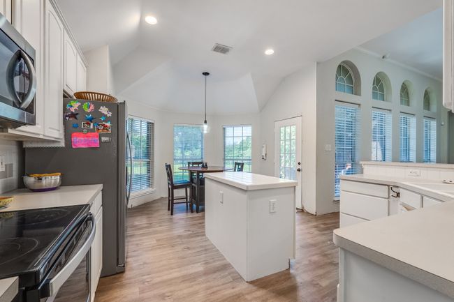 Kitchen with stainless steel microwave, white cabinetry, a center island, light wood-style flooring, and lofted ceiling | Image 21